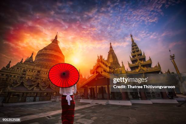 unidentified burmese woman holding traditional red umbrella and looks at golden shwezigon pagoda in bagan, myanmar - bagan photos et images de collection
