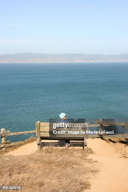 peaceful woman sitting on bench looking at view of the pacific ocean - female looking away from camera serious thinking outside natural stock-fotos und bilder