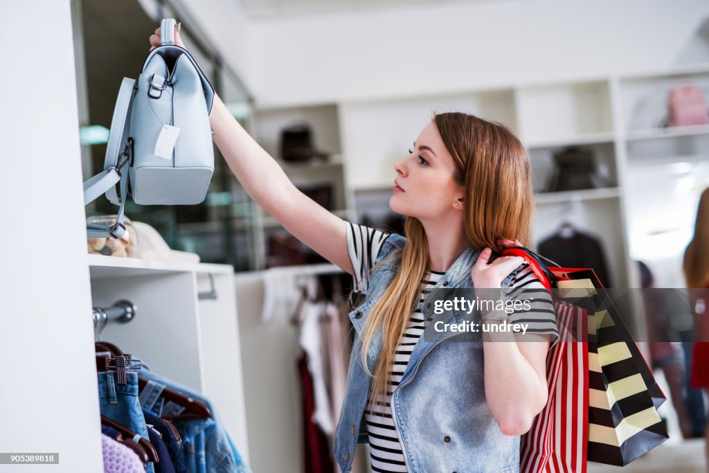 Young female shopper with shopping bags choosing the handbag matching her casual style