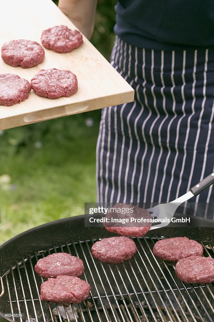 Man placing raw burgers on barbecue grill rack, close up, mid section