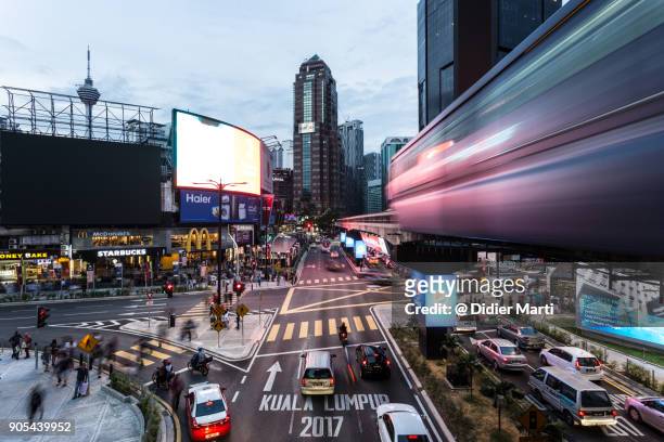 traffic and a monorail car rush through the bukit bintang intersection at night in kuala lumpur - kuala lumpur stock pictures, royalty-free photos & images