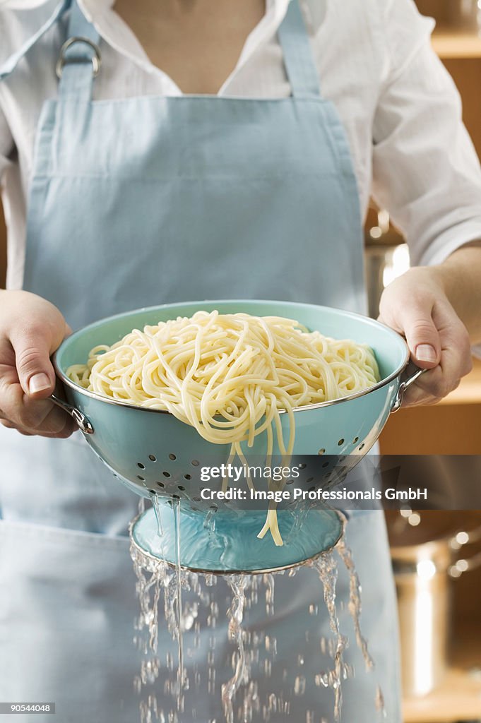 Woman draining cooked spaghetti, close up, mid section