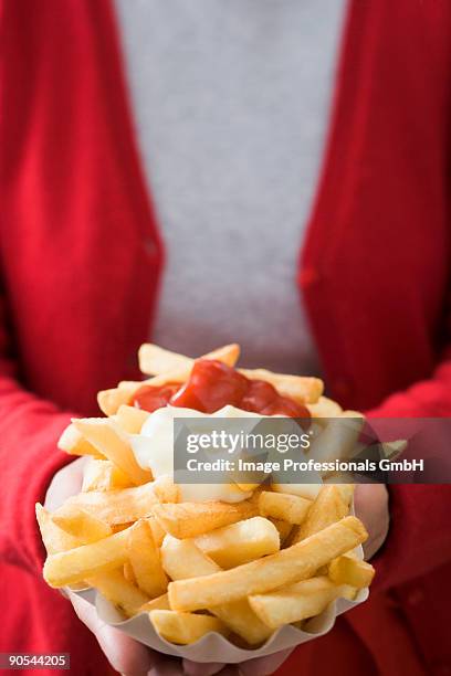 woman holding chips with ketchup and mayonnaise, mid section, close up - mayonnaise stock-fotos und bilder