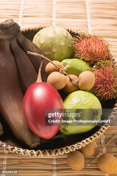 basket of tropical fruits on straw mat, close up - rieten mat stockfoto's en -beelden