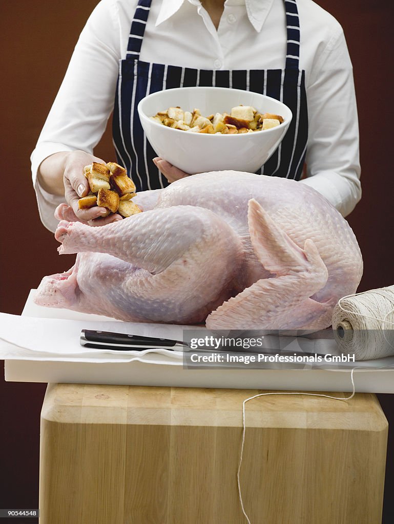 Person stuffing turkey with bread cubes, close up, mid section