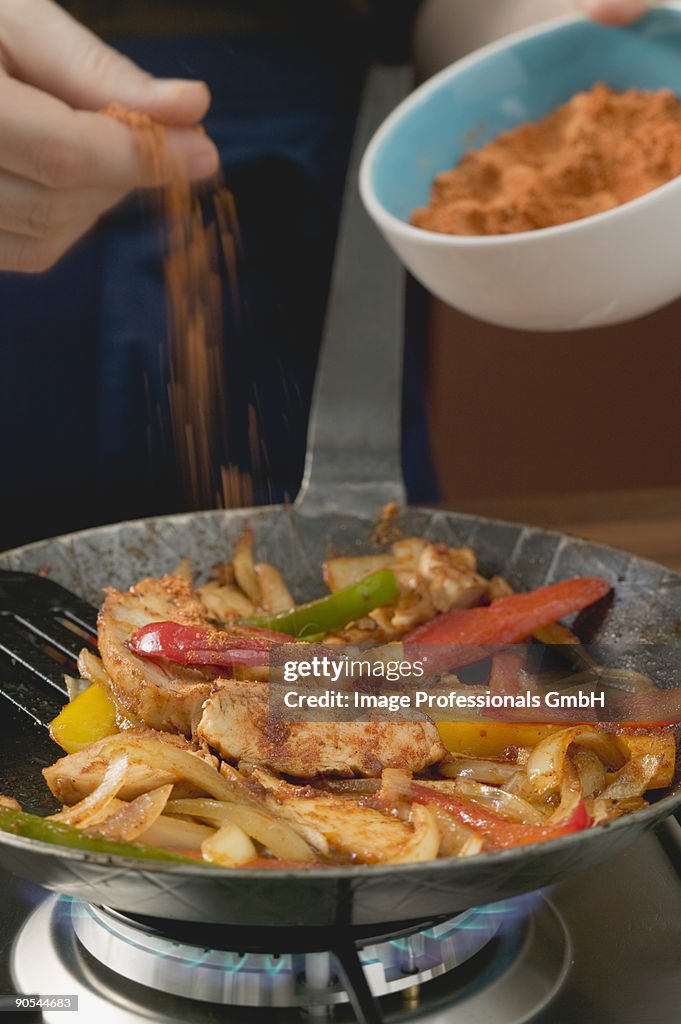 Adding chilli powder to chicken with onions and peppers, close up