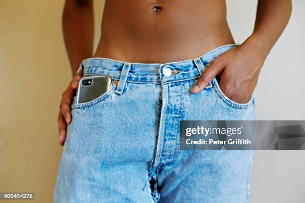 midsection of mixed race woman with cell phone in pocket of jeans - female navel ストックフォトと画像