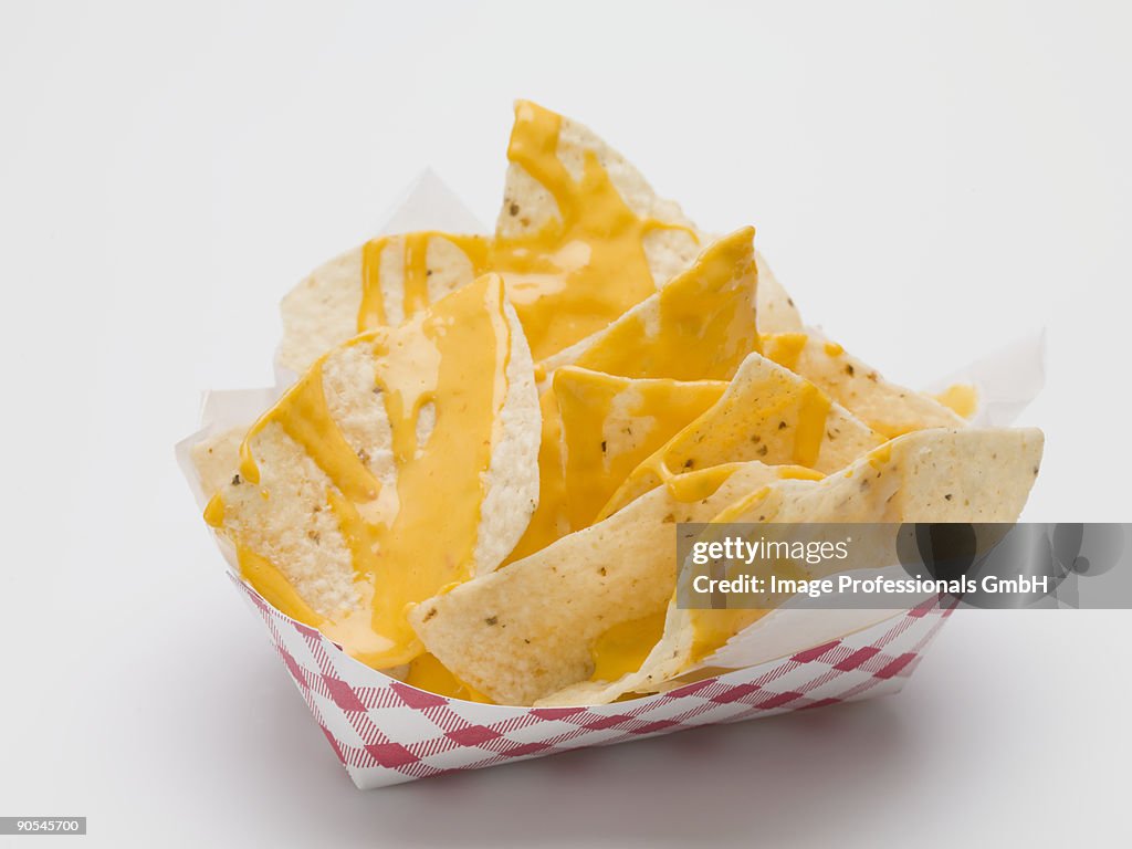 Nachos with cheese sauce in paper dish, close up