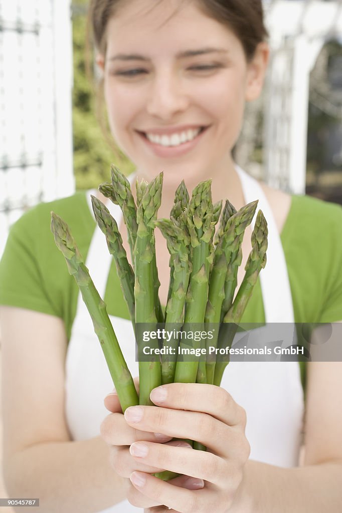 Young woman holding fresh green asparagus, smiling, close up