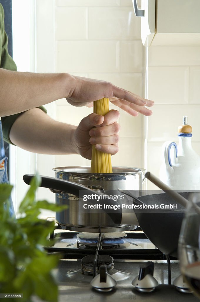 Human hand putting spaghetti into boiling water
