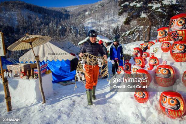 Man walks past traditional Japanese Daruma dolls placed in the snow as villagers work on building a shrine during preparations for the Nozawaonsen...