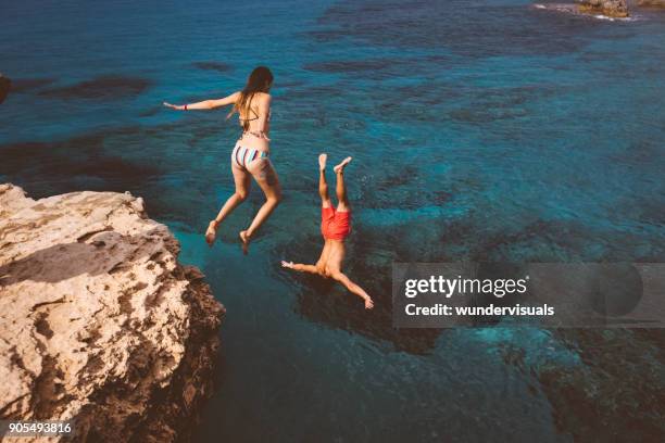 coppia attiva che si tuffa da un'alta scogliera nell'oceano - tuffi dalle rocce foto e immagini stock