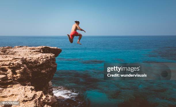 junge abenteuerlustige taucher sprung von klippe ins meer - cliff shore stock-fotos und bilder