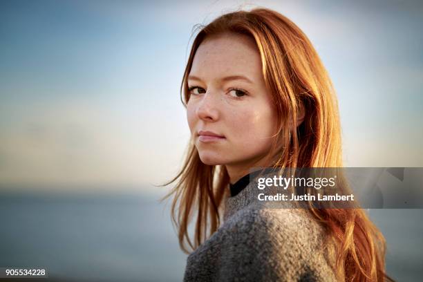 redhead teenager looking to camera in winter sunlight on beach - sorriso discreto imagens e fotografias de stock