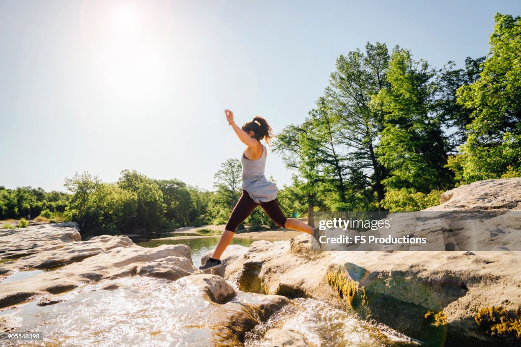 Caucasian woman jumping on rocks near river