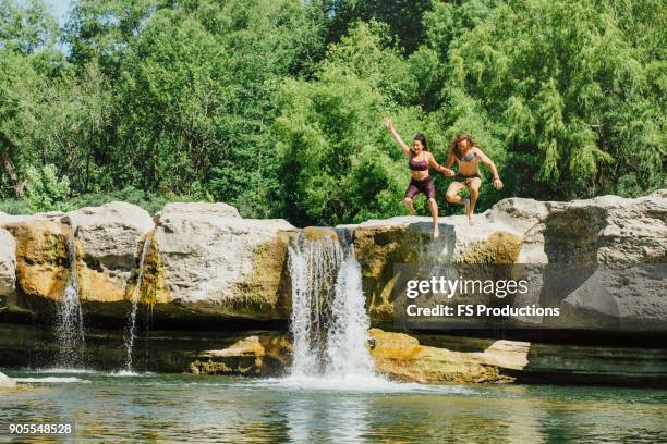 caucasian couple jumping off rocks near waterfalls - salto desde acantilado fotografías e imágenes de stock