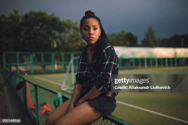 serious african american woman sitting on fence at sports field - real people serious not looking at camera not skiny stock pictures, royalty-free photos & images