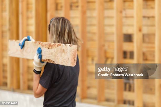 caucasian woman carrying lumber at construction site - carry foundation stock-fotos und bilder