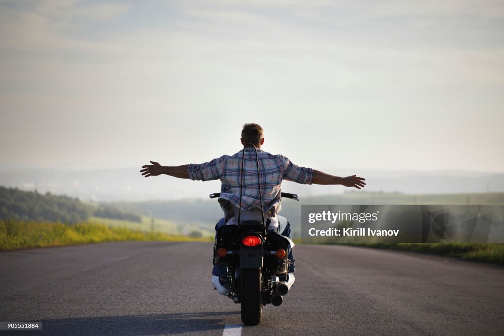 Caucasian man riding motorcycle with arms outstretched