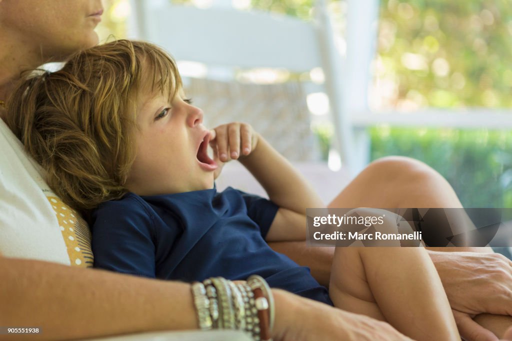 Caucasian boy yawning in the lap of mother