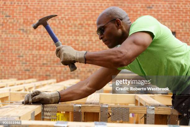 black man hammering nail at construction site - hammer and nail fotografías e imágenes de stock