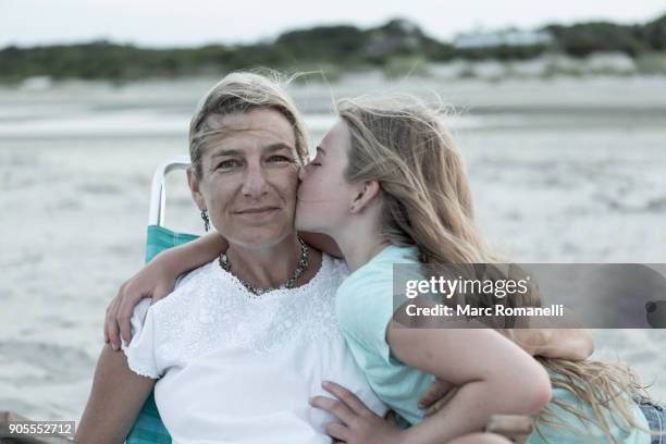 caucasian girl kissing mother on cheek at windy beach - friends kissing cheeks fotografías e imágenes de stock