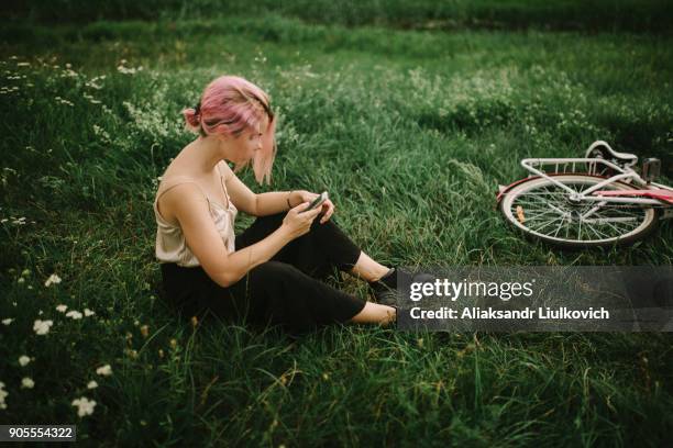 caucasian woman sitting infield texting on cell phone - dyed red hair fotografías e imágenes de stock