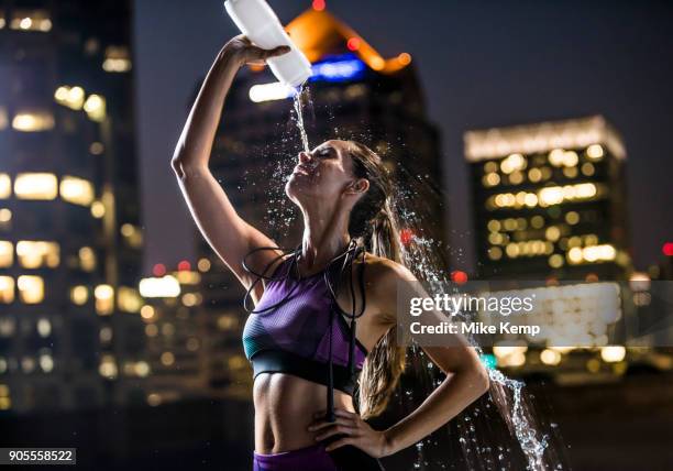 caucasian woman spraying water on face in city at night - water bottle splash stock pictures, royalty-free photos & images