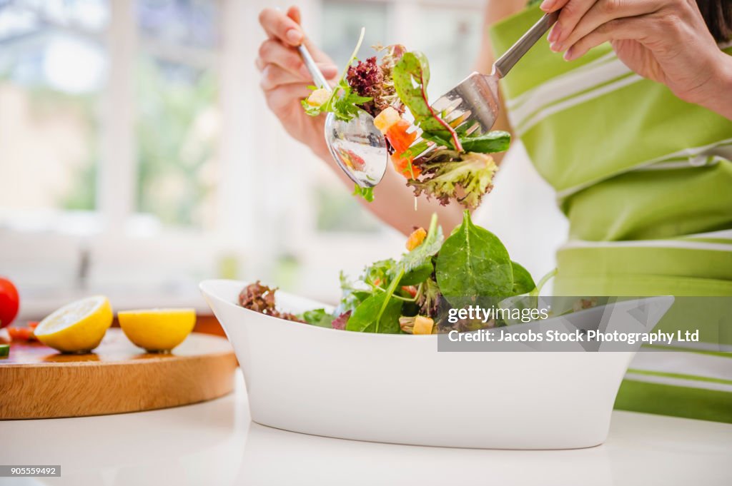 Hispanic woman tossing salad in domestic kitchen