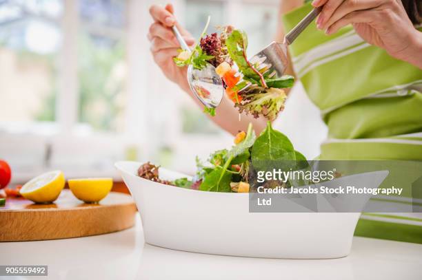 hispanic woman tossing salad in domestic kitchen - mixing stock pictures, royalty-free photos & images