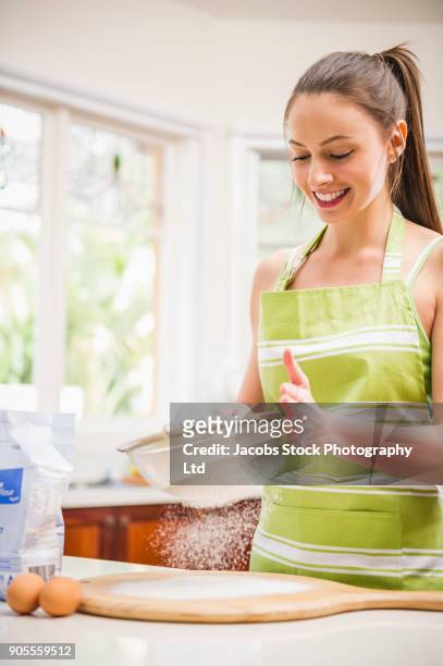 smiling hispanic woman sifting flour in domestic kitchen - flour sifter stock pictures, royalty-free photos & images