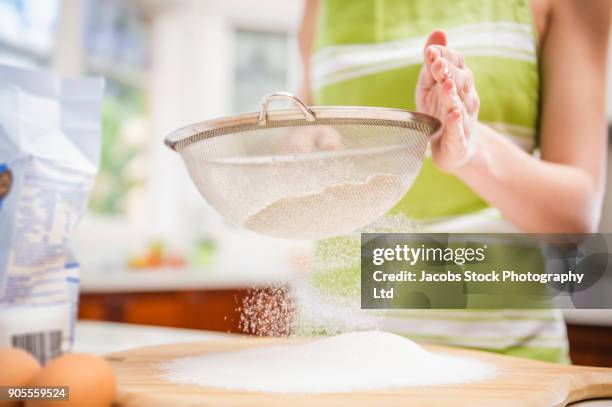 hispanic woman sifting flour in domestic kitchen - sifting stock pictures, royalty-free photos & images