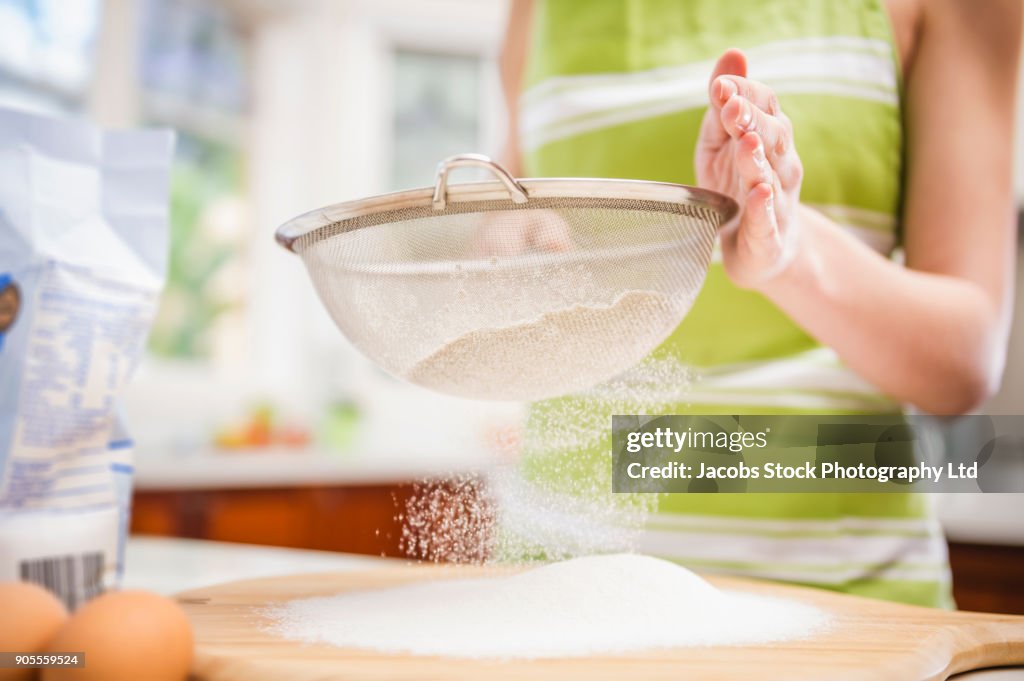Hispanic woman sifting flour in domestic kitchen