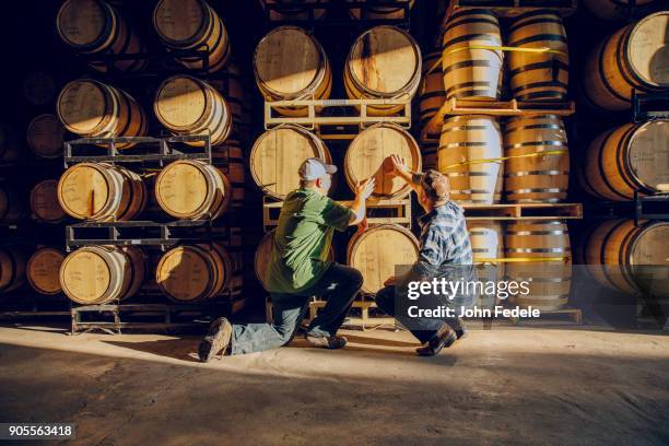caucasian men examining barrel in distillery - destillation stock-fotos und bilder