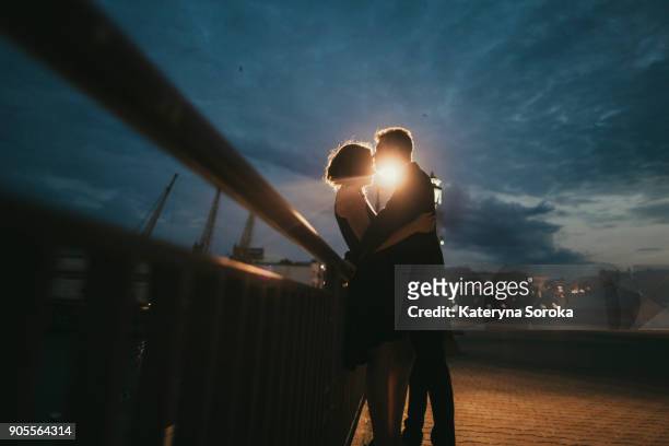 caucasian couple kissing near railing at night - romance stock pictures, royalty-free photos & images
