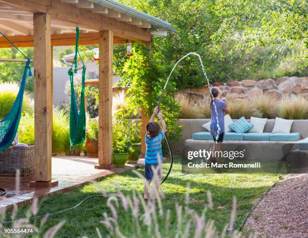 caucasian boy spraying sister with hose in backyard - lamy new mexico stock pictures, royalty-free photos & images
