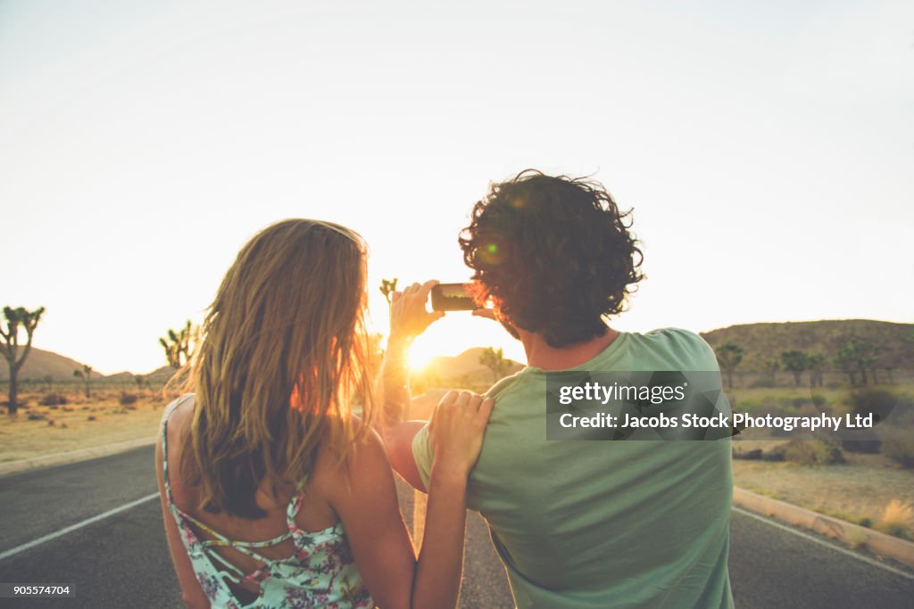 Hispanic couple photographing sunset in street