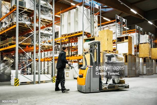 warehouse worker maneuvering forklift stacked with items for storage - pallet jack stock pictures, royalty-free photos & images