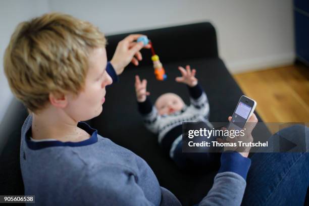 Berlin, Germany Symbolic photo on the topic of education: A young mother looks at her smartphone while her child is playing on January 16, 2018 in...