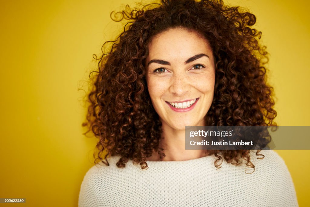 Curly haired mixed race woman smiling openly at camera on vibrant yellow backdrop