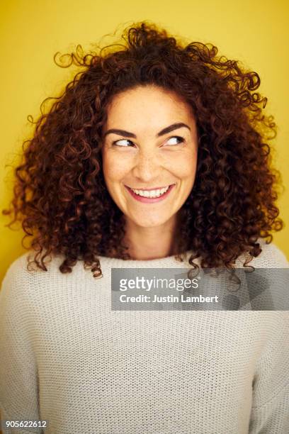 young curly haired woman looking off camera with a cheeky big smile - regard de côté studio photos et images de collection