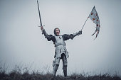 Girl in image of Jeanne d'Arc stands in armor and issues battle cry with sword raised up and flag in her hands.