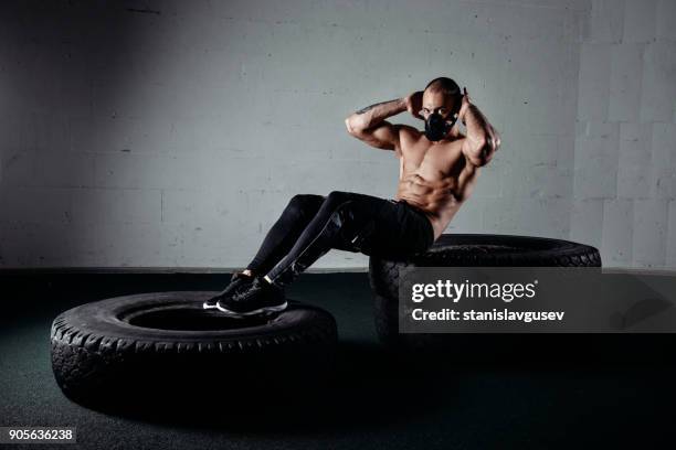 portrait of a man wearing an elevation mask sitting on tyres doing sit ups - tyre side view foto e immagini stock