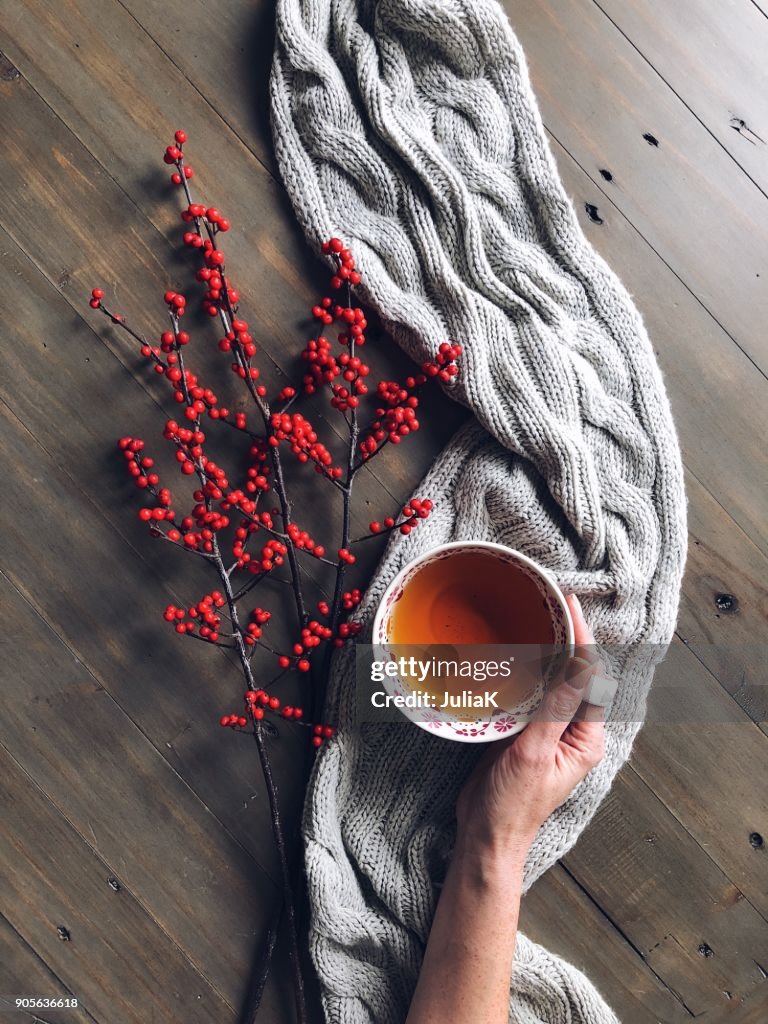 Womans hand holding a cup of herbal tea with berries and a knitted scarf