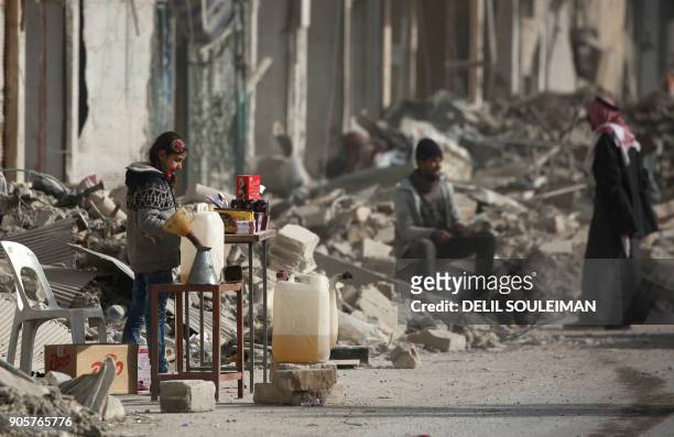 Syrian girl sells items amidst the debris of destroyed buildings in the northern Syrian city of Raqa, on January 11, 2018 after a huge military...