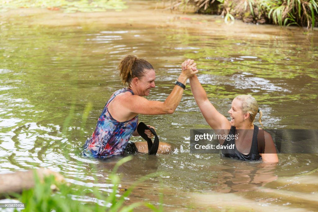 Athletic Mature Women Helping Each Other in a River During an Obstacle Course Mud Run