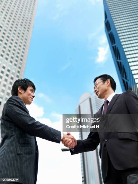 two businessmen who shake hands - low angle view of two businessmen standing face to face outdoors stock pictures, royalty-free photos & images