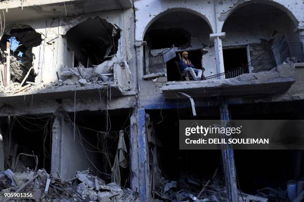 Syrian man sits on the balcony of a damaged building in the northern Syrian city of Raqa, on January 16, 2018 after a huge military operation led on...