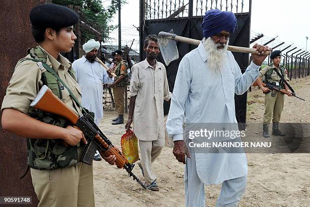 Indian Border Security Force personnel stand guard alongside a barbed wire fence as farmers walk to their fields at a checkpost at Roranwala near The...