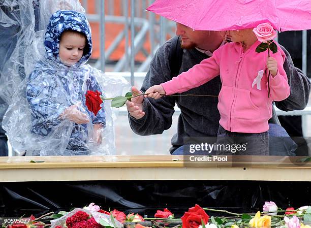 Young girl and boy with a man squats in the rain at the reflecting pool placing flowers as people gather at Ground Zero during a 9/11 memorial...